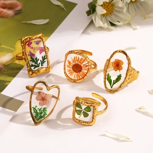 Golden open rings with preserved dried flowers in resin, set of five shapes on white background
