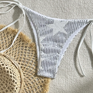 Close-up of white sequined bikini bottoms with side ties on a white textured rug