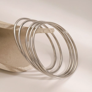 Close-up of sleek silver stainless steel bangles set against a beige stone backdrop
