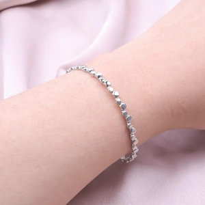 Close-up of a delicate silver C-shaped stainless steel bracelet with geometric beads