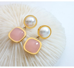 Macro detail of gold drop earrings featuring white round pearl and pink square stone charm