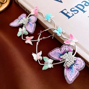 Close-up of oversized purple embroidered butterfly hoop earrings with sparkling rhinestones