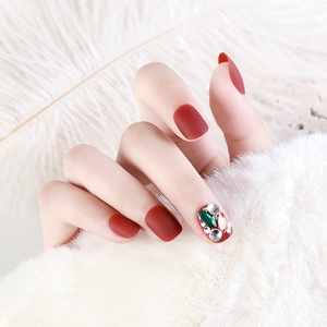 Matte burgundy press-on nails featuring sparkling rhinestones and green gemstone accents