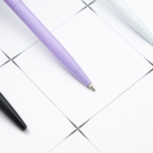 Creative purple fluffy pom pom ballpoint pen on minimalist white grid paper background