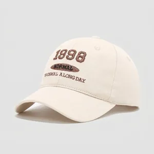 Dettaglio del ricamo 3D con scritta 1998 su un cappellino in cotone color crema