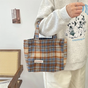 Detailed close-up of a vintage plaid canvas tote bag with woven logo and carry handles