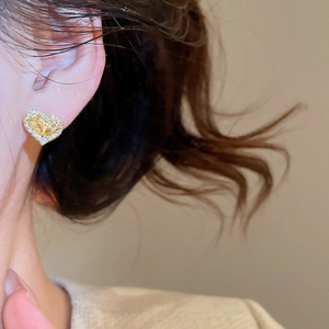Close-up of heart-shaped gold-plated stud earring with sparkling zircons on model ear