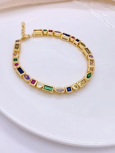 Detail shot of golden bracelet with colorful geometric zircons on a white round plate