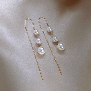 Detailed close-up of golden tassel threader earrings with three gradient pearls on satin