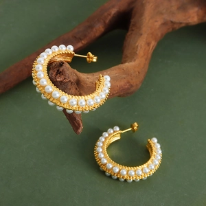 Elegant gold-plated C-shaped hoop earrings with double row pearl inlay on dark wood