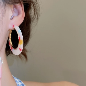 Close-up of C-shaped resin earrings with colorful flecks and golden metal accents