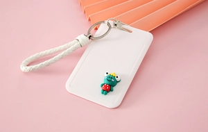 Detail of white sliding card holder with woven hand strap and green cartoon frog motif