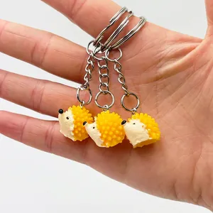 Three cute yellow hedgehog resin keychains held in palm over white background
