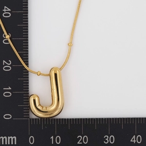 Macro detail of puffy letter J gold necklace with measurement scale for size reference