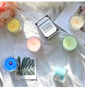 Artistic overhead shot of colorful scented candles in glass jars on white wrinkled fabric