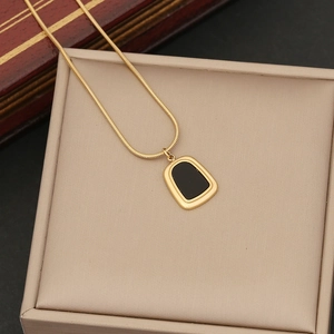 Macro shot of gold snake chain with black trapezoid pendant on jewelry box