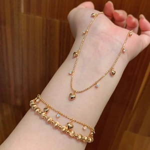 Dettaglio macro del bracciale dorato con ciondolo a cuore e zirconi sul polso
