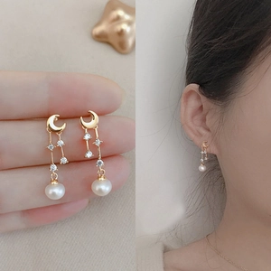 Detail of gold crescent moon earrings with dangling small zircons and white freshwater pearl