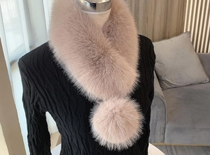 Detail of white faux fur collar with large pompom tie on a black knitted garment