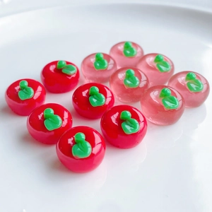 Miniature resin apple charms in red and pink arranged in a triangular array on a white plate