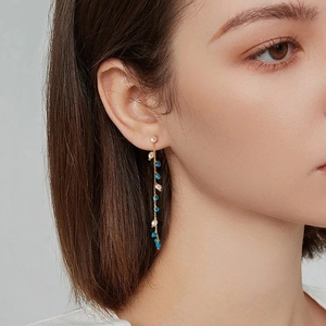 Detail of long gold tassel earrings with pearls and blue beads worn by a model
