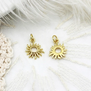 Detailed close-up of two mini golden sun pendants with hanging rings on lace and feathers