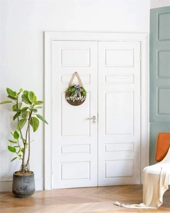 Detail of a round wooden welcome sign with greenery and checkered bow on a white door