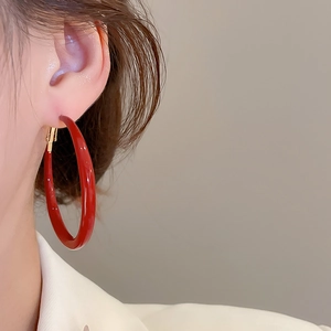 Close-up of large round red enamel hoop earring with gold hinge worn by a model