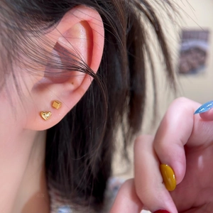 Macro shot of minimalist gold-plated heart and cube stud earrings worn on the earlobe