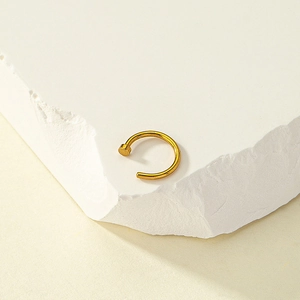 Detailed view of a golden non-piercing nose ring resting on a white textured stone