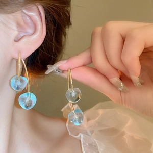 Close-up of translucent light blue heart dangle earrings worn by a model in soft light