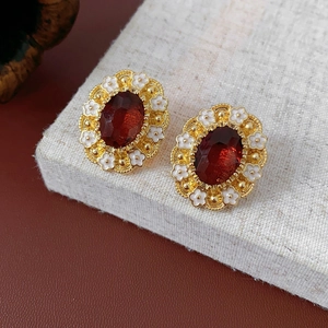 Macro detail of vintage floral earrings with dark red gemstone on beige linen background