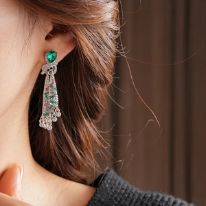 Close-up of vintage drop earrings with green teardrop gem and colorful crystal fringe