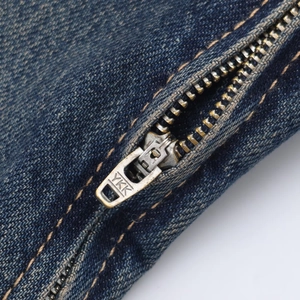 Detailed close-up of a YKK metal zipper on a washed blue denim dress with orange stitching