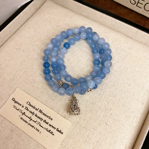 Macro detail of multilayer blue bead bracelet featuring a silver money bag charm with engraving