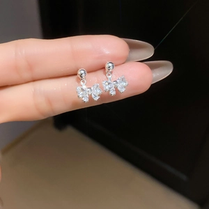Close-up of fingers holding silver bow earrings with sparkling white zircons