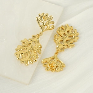 Polished gold earrings with organic leaf design on white marble surface