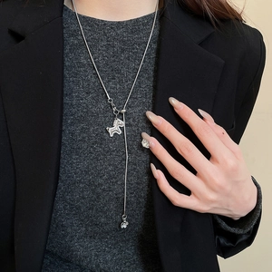 Close-up of silver pony and flower pendant necklace on model's charcoal knit sweater
