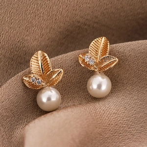 Elegant gold leaf earrings with white pearls and sparkling zircons on khaki silk background