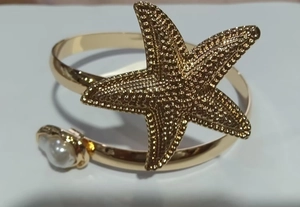 Close-up of golden starfish arm cuff featuring a white imitation pearl and textured details