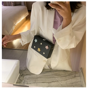 Detail of a black square chain bag with 3D colorful flowers shown in a mirror selfie
