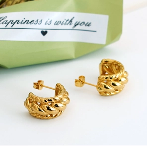 Detail of chunky gold-plated twisted hoop earrings with a high-polished mirror finish