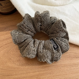 Close-up of olive green knitted scrunchie with scalloped lace and fashion label