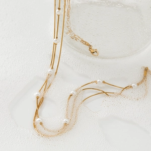 Elegant gold multi-layer necklace with white pearls and snake chain on a soft white background