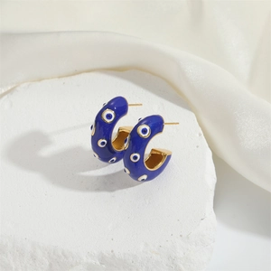 Detail of blue enamel C-shaped evil eye hoop earrings on white stone surface