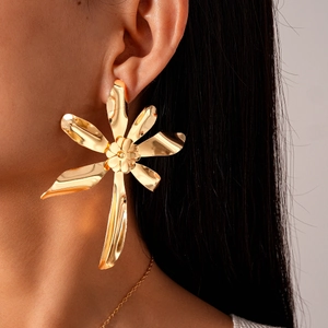 Close-up of a model wearing large golden flower statement earrings with a metallic finish