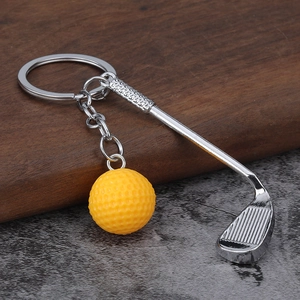Close-up of a mini golf club and yellow golf ball keychain on a marble and wood surface