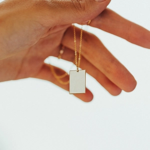 Collier à pendentif carré minimaliste en acier inoxydable plaqué or tenu à la main