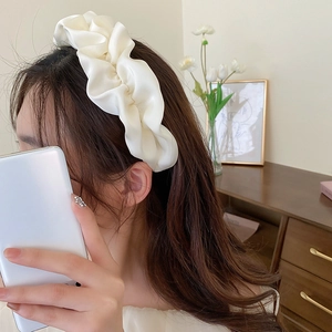 Detail of elegant creamy white pleated satin headband on model in a warm indoor setting