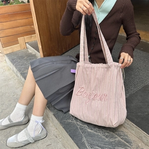 Detail of pink striped canvas tote bag with Bonjour embroidery shown in a lifestyle setting